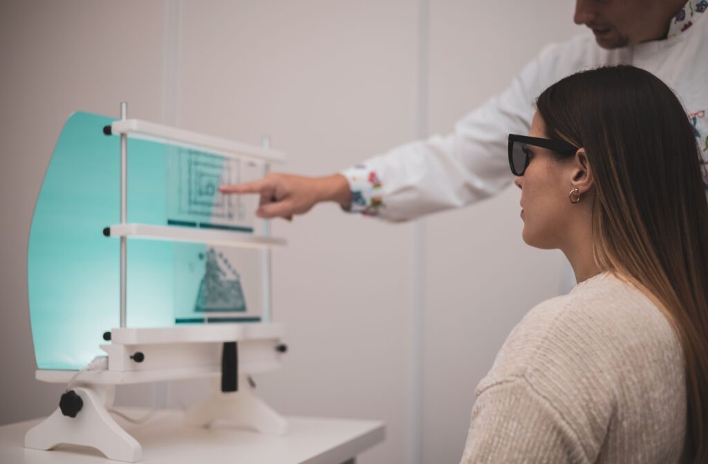 A woman wearing dark glasses and looking at a vision therapy diagram as her eye doctor points to it.