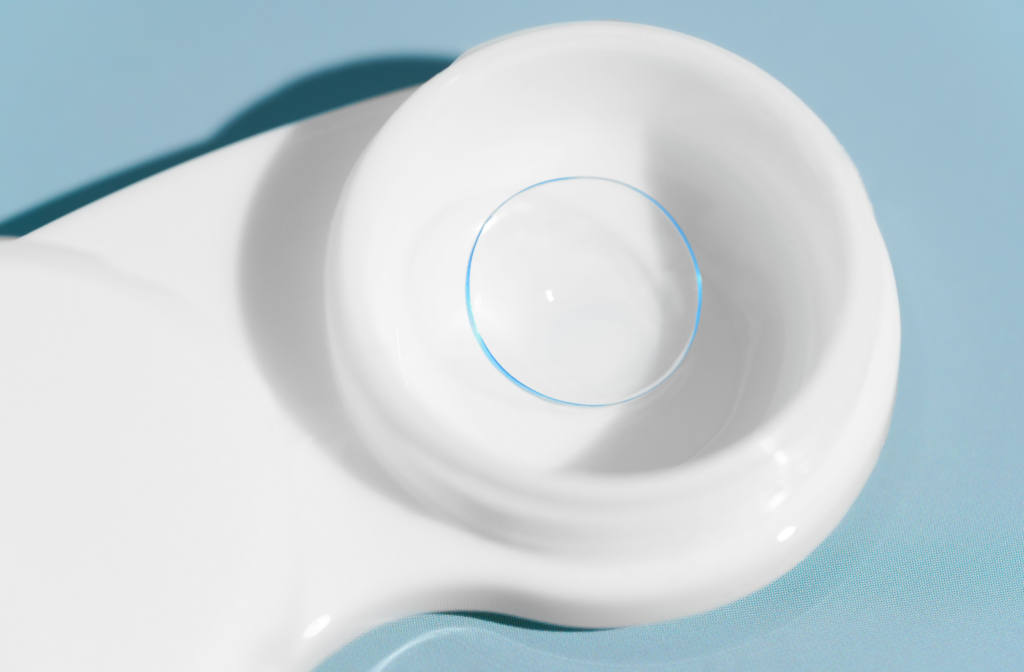 A white, unmarked lens case holds a singular contact lens in solution.