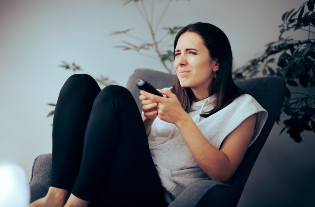 Woman squinting at a TV screen while holding a remote, indicating difficulty seeing clearly.