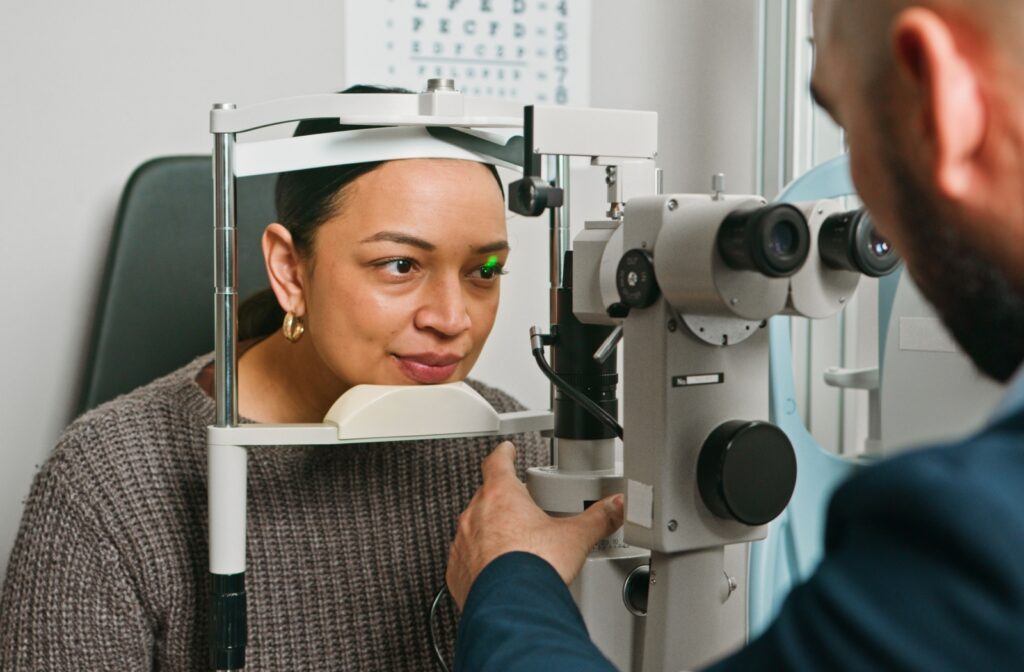 Patient resting head in diagnostic eye exam tool with green laser aimed at one eye during testing.