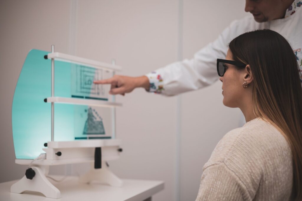 Woman wearing therapeutic glasses during vision therapy session with specialized equipment at optometry clinic.