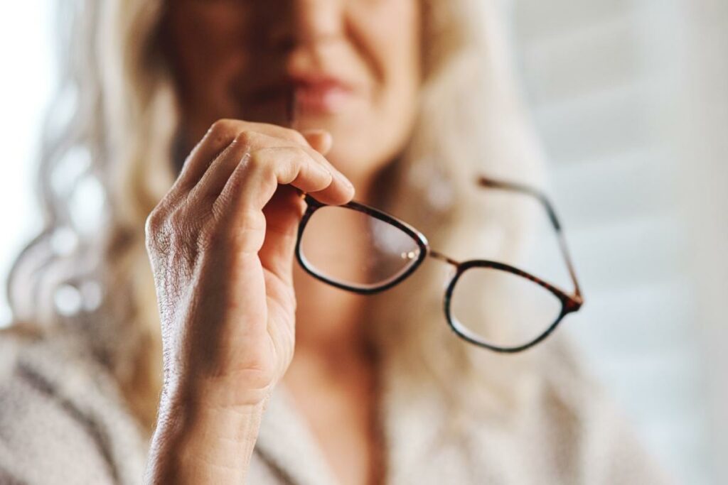 Older woman holding her glasses just below her face.